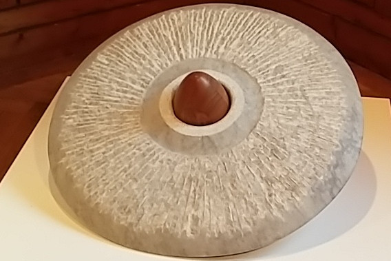 Bildhauerarbeit aus Stein: radförmige Scheibe, in der Mitte ein Ei aus Holz