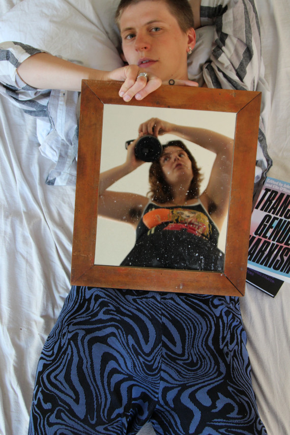 Simone Körner liegt auf Bett und hält vor ihren Oberkörper einen Spiegel. Darauf zu sehen: eine junge Frau mit einer Glocke in den Händen