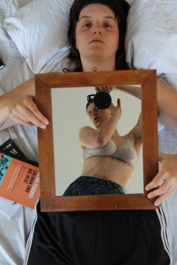 Veronika Haller liegt auf Bett und hält vor ihren Oberkörper einen Spiegel. Darauf zu sehen: eine junge Frau, tanzend, bekleidet mit Hose und Büstenhalter
